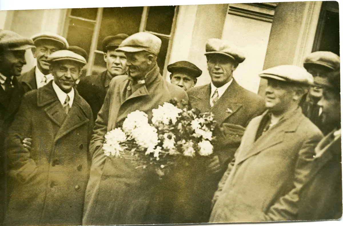 En gruppe menn med sixpence lue. Hans Engnestangen holder en blomsterbukket.