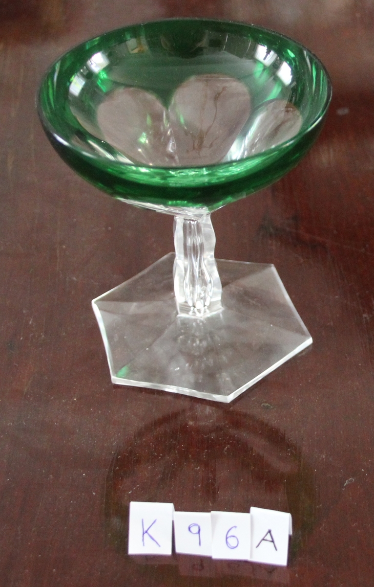 Glass med sekskantet fot, stetten litt innsnevret på midten, skålen har sekspæreformede fasetter, sett ovenfra som en seksbladet blomst.