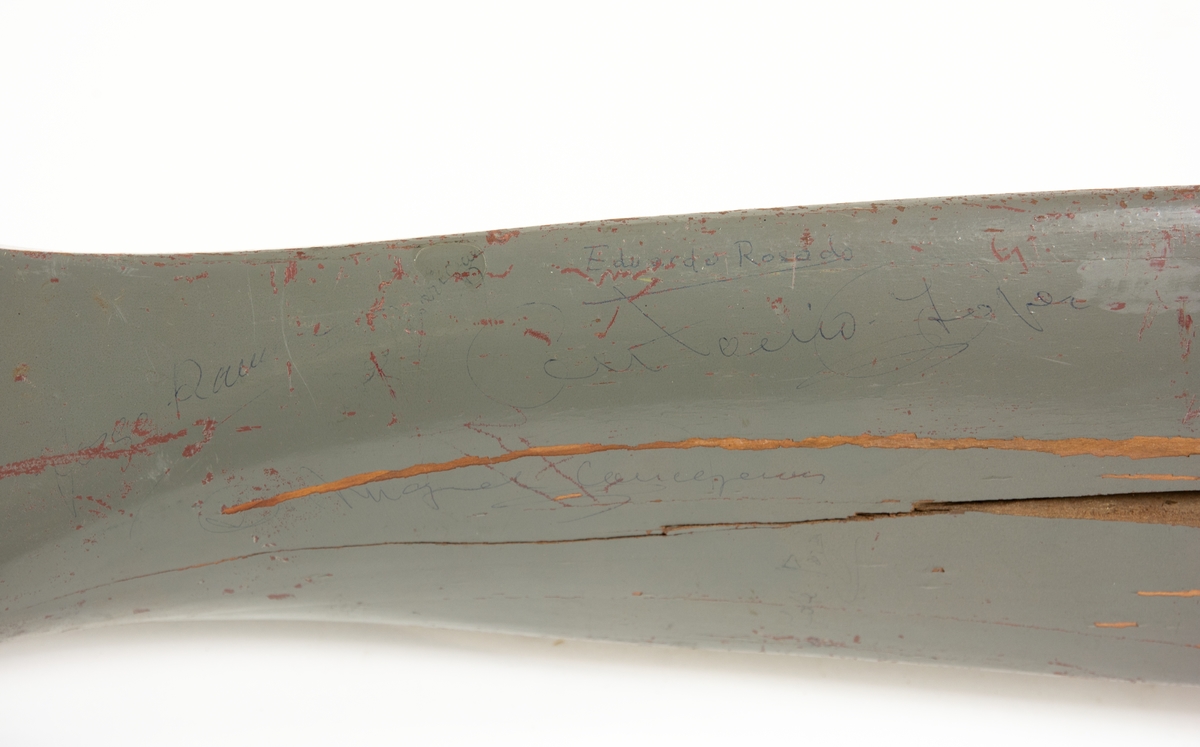 Gråmålad tvåbladig propeller av trä. Propellern är försedd med ett antal handskrivna autografer.