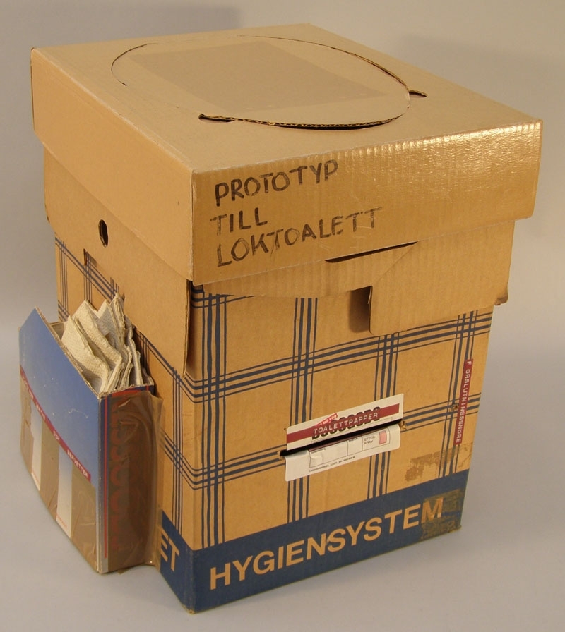 Prototyp till loktoalett (vilket också står skrivet med tuschpenna på locket) i form av en låda i papp med avtagbart lock, locket i papp har en plastad yta och ett öppningsbart "toalettlock". På lådans sida tejpat en behållare i papp märkt: "PLATS FÖR LEKTYR OCH SERVETTER" som det ligger pappersservetter i märkta "InterCity". Framtill på lådan märkt "TOALETTPAPPER" med en skåra under (för att dra fram toalettpapper), toalettpappersrulle märkt "SJ" ligger i lådan. Baktill på lådan en användarbeskrivning i tre steg, med texten upptill "PLAST-DO-SET Bruksanvisning", vilket enligt en förslutningsbar säck är tänkt att användas i lådan för avträdet.