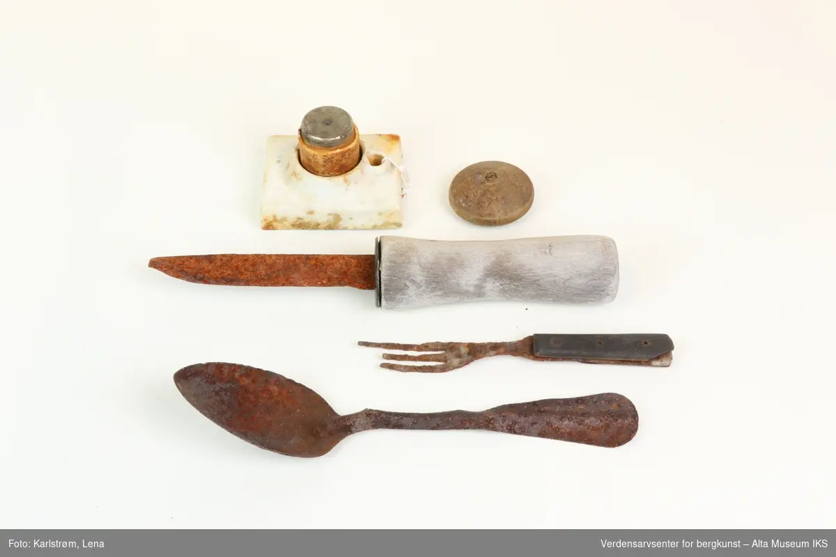 Samling husgeråd funnet ved Nordlysobservatoriet på Haldde: Kniv og gaffel med trehåndtak, metallskje, sikring i porselen og metall, lite rundt trobjekt.