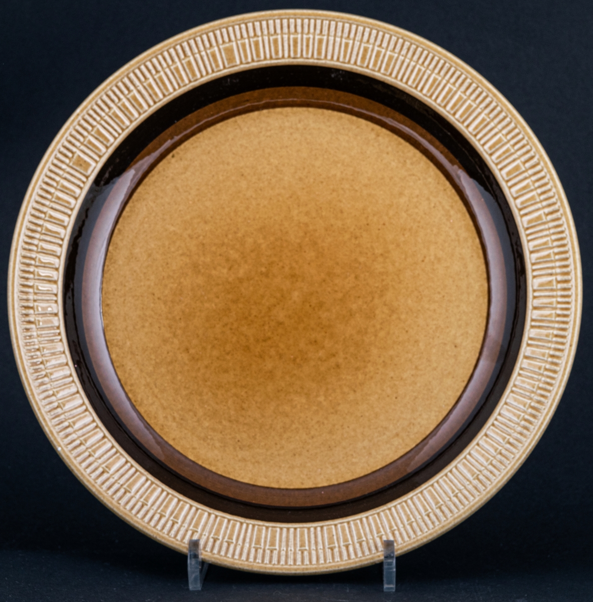Tallrik, flat tillhörande servisen Terra, ljusbrun bottenglasyr med två mörkare band i brunt samt en reliefdekor ytterst på brättet.
Design av Berit Ternell.