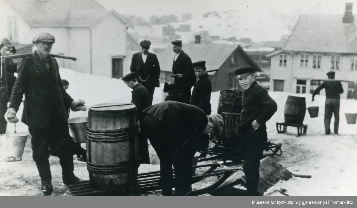 Honningsvåg. Vinter. Vann hentes i Tokleelva. Menn og gutter med bøtter og vanntønner på kjelke. Ca. 1921.