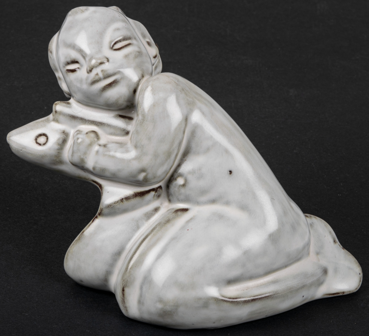 Figurin i stengods och glasyr 2560, Pojke med fisk, formgiven av Maggie Wibom, producerad av Gefle Porslin 1933.