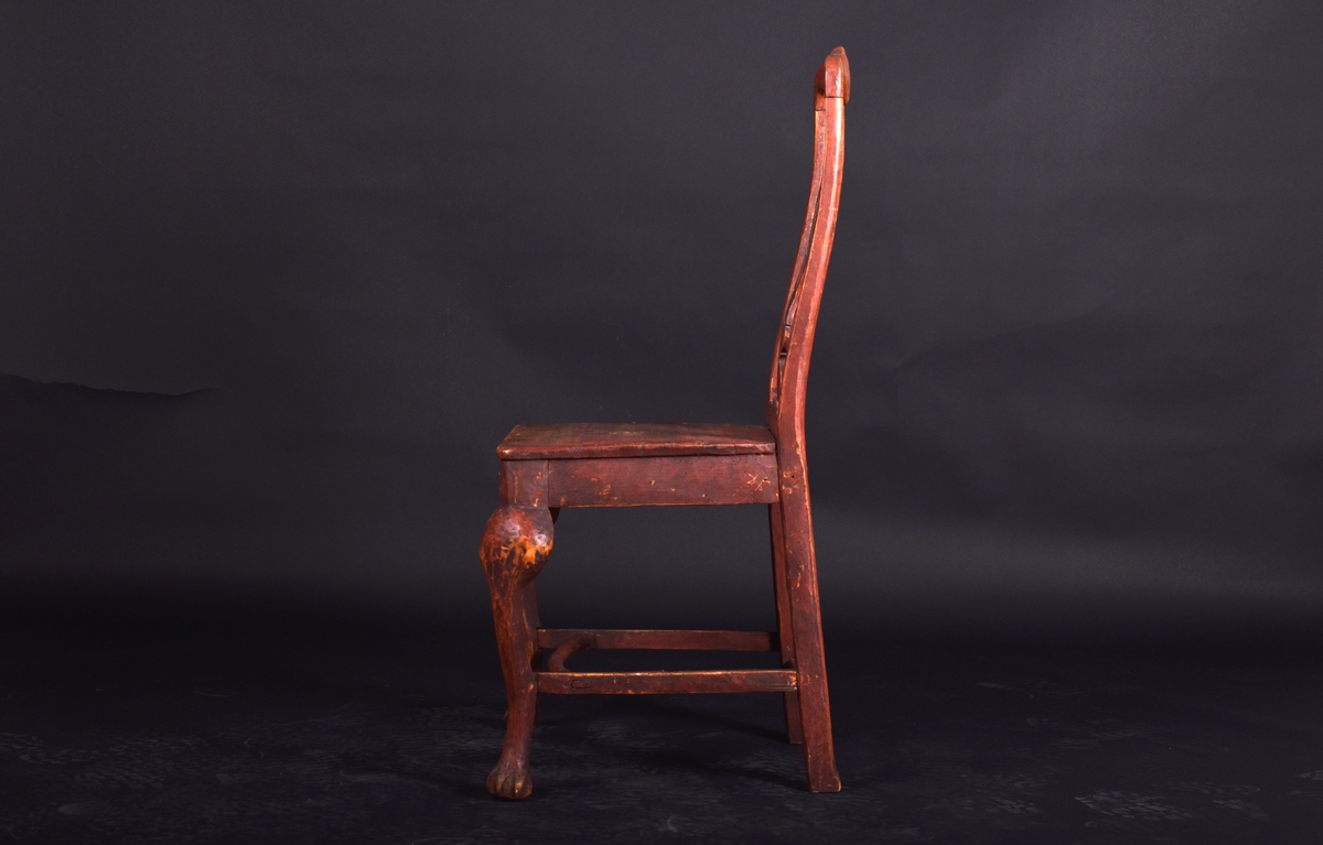 Stol av björk och furu, på fyra svängda ben. Ryggen har en mittbricka i balusterform. Stolen är målad i mörkt rött och ryggbrickan har målad dekoration i rokokostil i grått och vitt.