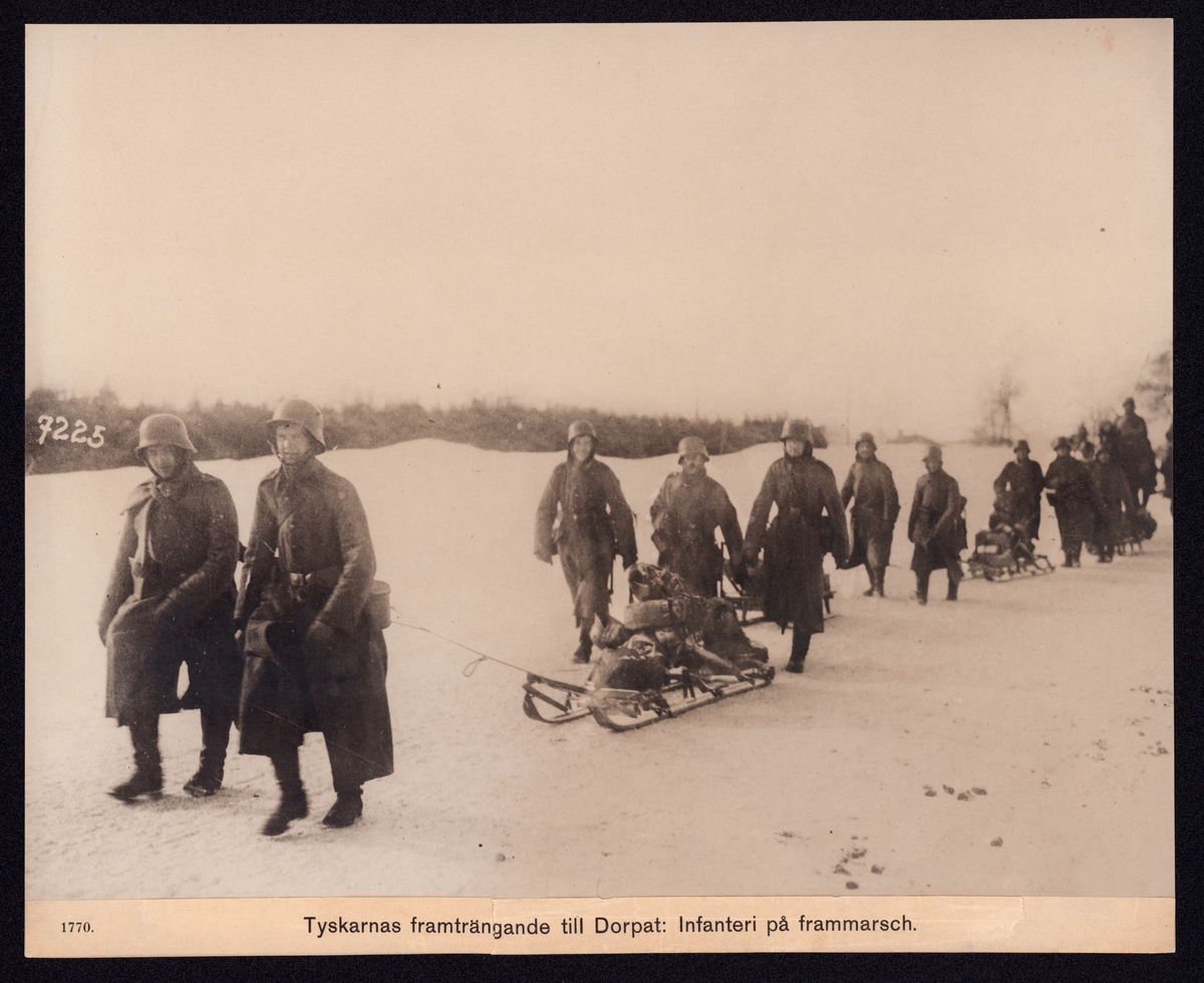 På bilden syns en kolonn soldater på frammarsch under vintertid. Soldaterna dra sin utrustning på slädar.