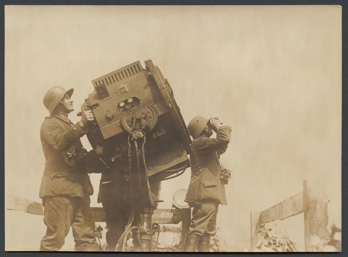 Bilden visar två soldater som arbetar med en stor strålkastare. Den ena av de iaktar himmelen med en kikare.