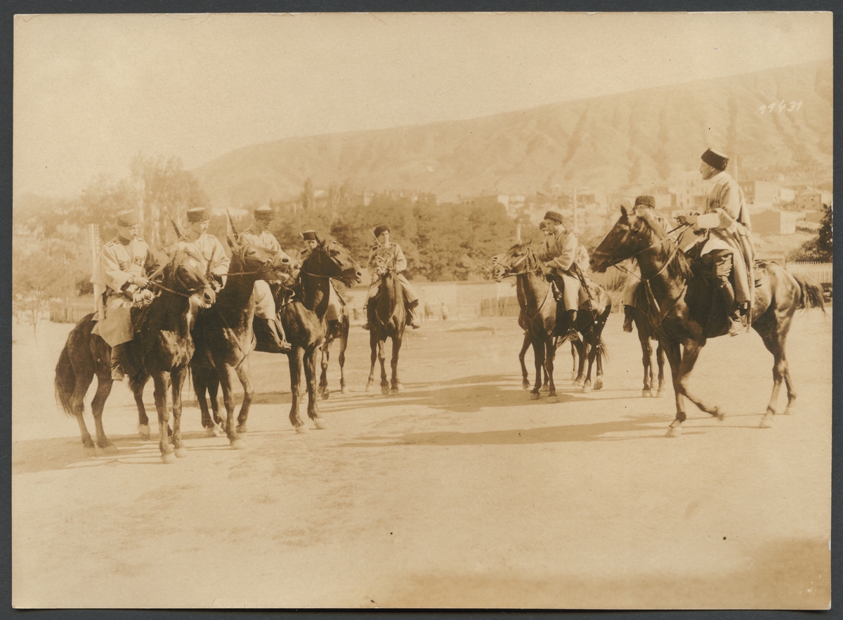 Bilden visar uniformerade män med gevär och pälsmössor till häst. I bakgrunden syns en bergskedja.