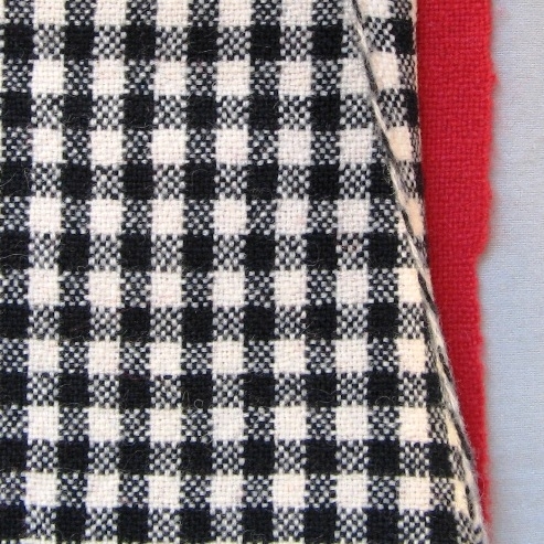 Vävprov till beklädnadstyg vävt i dubbelväv i tuskaft med avbindetråd i ullgarn, stickgarn 8/2. Vävprovet består av två skilda lager som punktvis är fästade vid varandra genom avbindetråden. Det ena lagret är enfärgat rött och det andra rutigt i svart och vitt. Vävprovet har beretts genom lätt valkning och pressning samt lätt ruggning av den röda sidan. Vävprovet har en 50mm  respektive 65mm bred handfåll i vardera kortsidan. 

Vävprovet med modellnamn Duffe är formgivet av Ann-Mari Nilsson och tillverkat av Länshemslöjden Skaraborg. Det finns ett vävprov monterat i aluminiumram, se inv.nr. 0041:13, som finns med på sidan 80-81 i vävboken Väv tyger till kläder av Ann-Mari Nilsson i samarbete med Länshemslöjden Skaraborg från 1989, ICA Bokförlag. Tyget är enligt boken lämpligt att använda till jacka eller kappa. Se även inv.nr 0041-0096 ur samma bok.