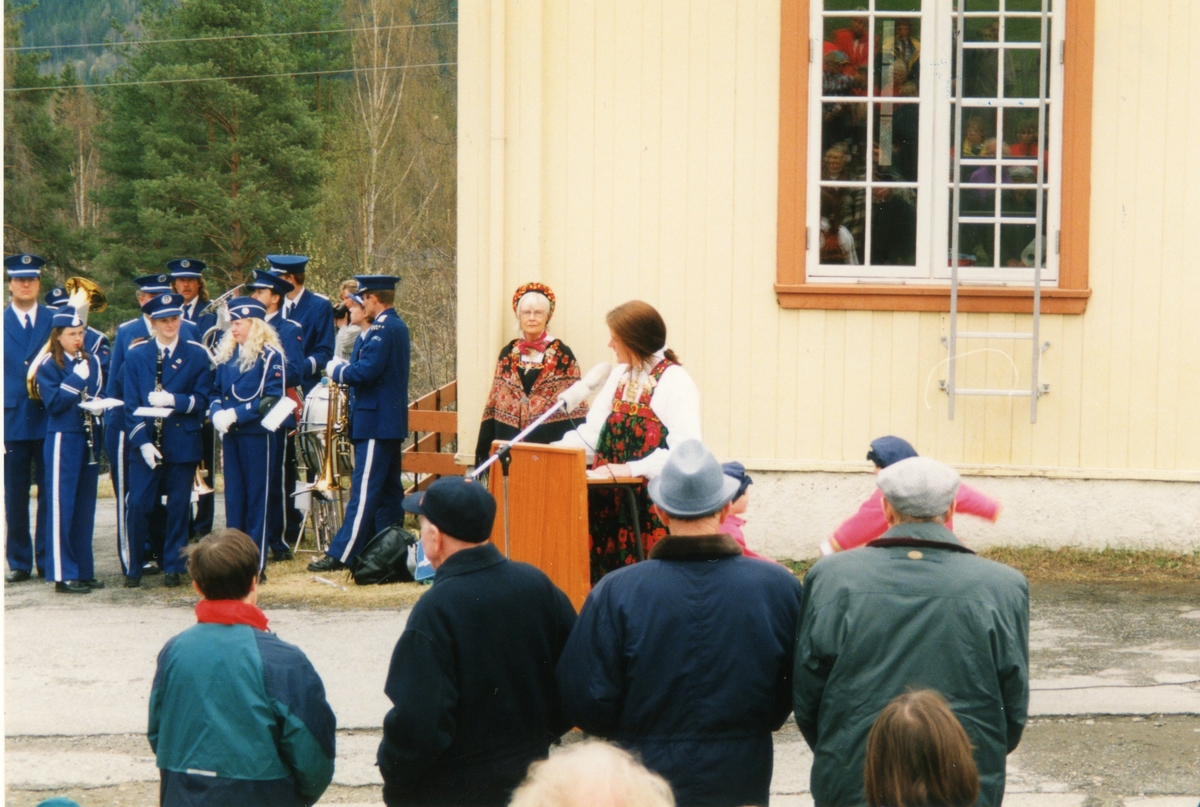 Gruppe,bunad,musikkuniform.
Guri Bråten er på talarstolen og Gudrun Larsgard Bøthun står til venstre for talarstolen.
