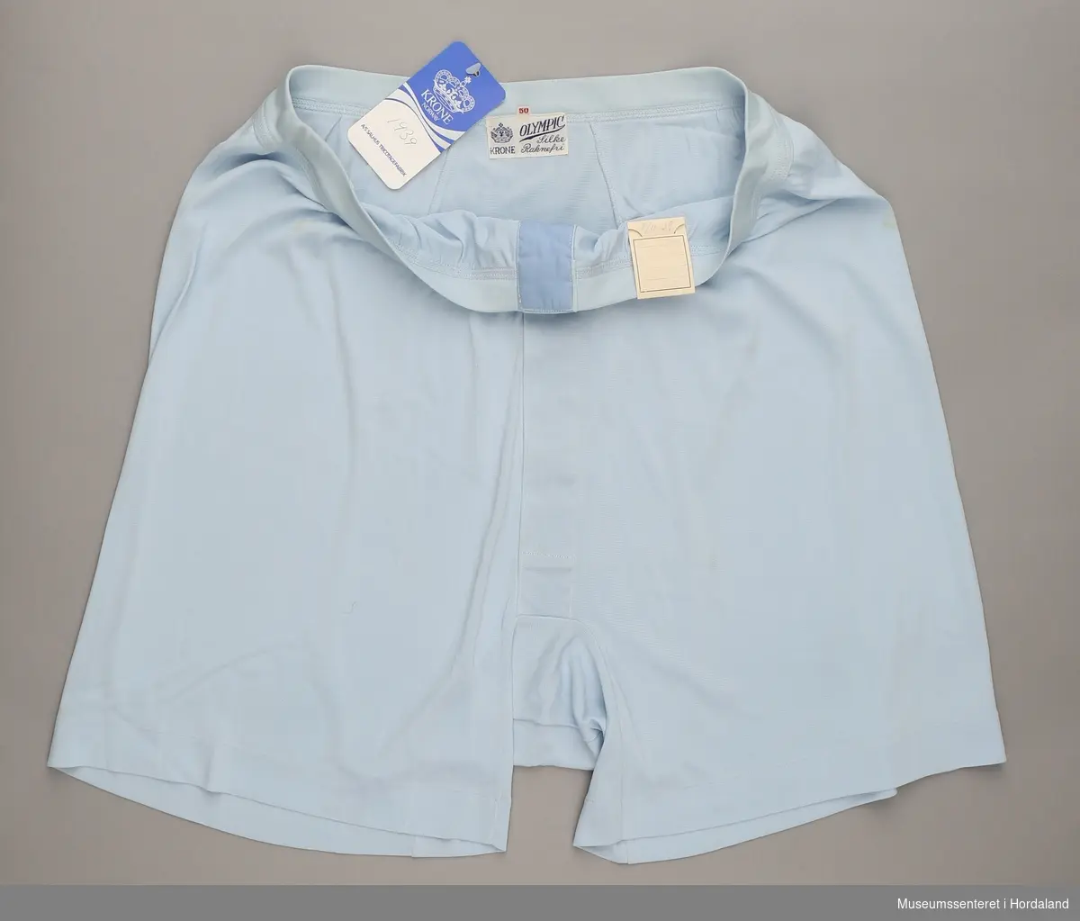 Lys blå underbukse i kortbukseform i merket Krone Olympic, med opning framme. Angiveleg strikka i "raknefri" silke.