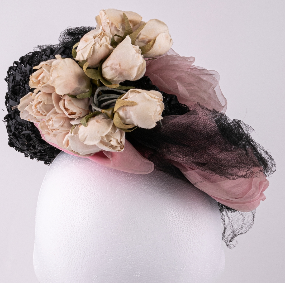 Hatt av svarta pärlor, garnerad med skära rosenknoppar, rosa chiffong, svart tyll och stenkolsspänne.