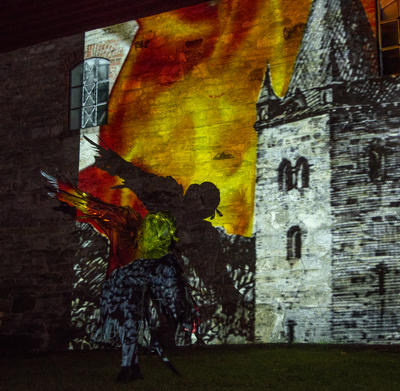 En svart fugl flyr foran en videoprojeksjon av middelalderkatedralen som brenner. (Foto/Photo)