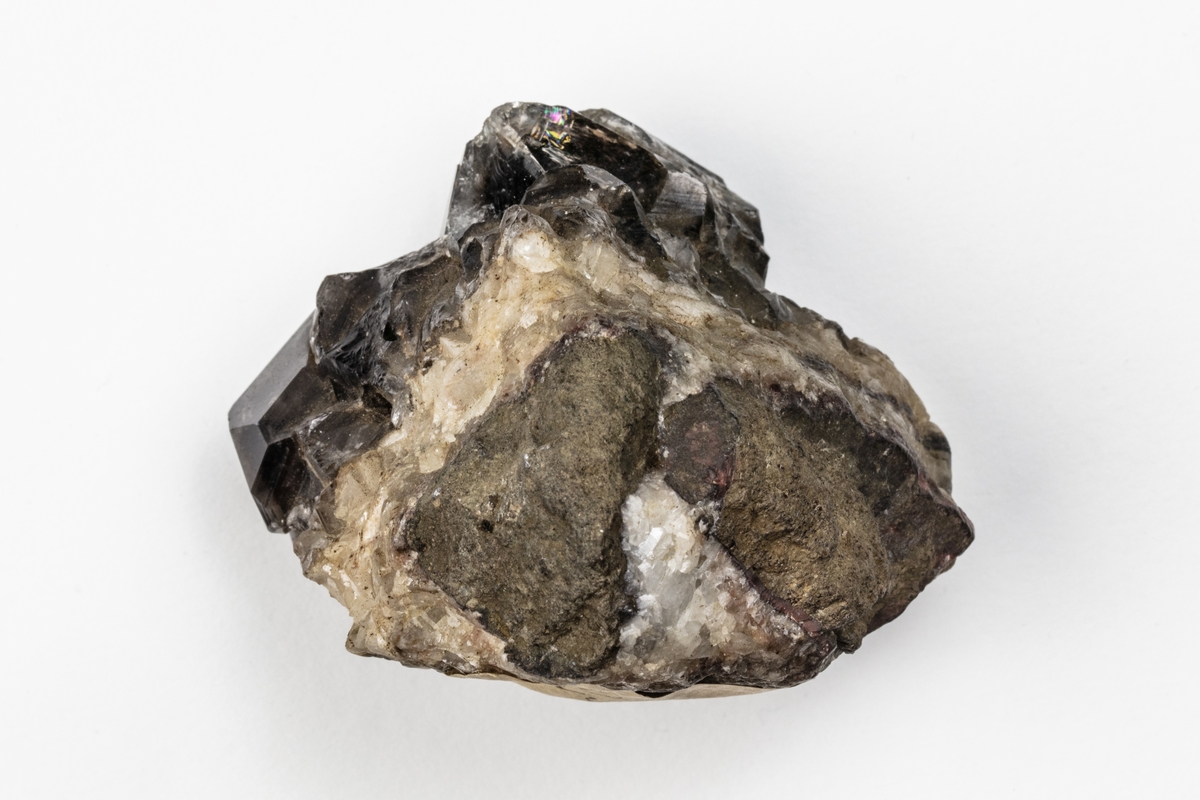 Ett mineral som är en kvarts och består av kiseldioxid. Kvartsen har kristallform och färgen är mörk, rökfärgad. Exemplaret kommer från Hässelkulla i Närke, Sverige.