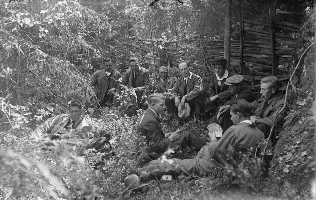 Skytterstevne på Tretten våren 1931. En gruppe menn spiller kort i skogen. Karl Olav Moe sitter i bakgrunnen.