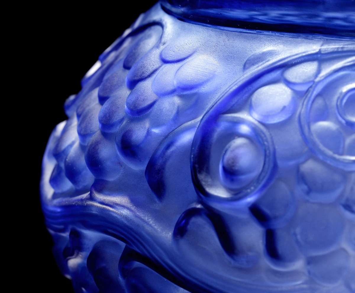 Halvopak blå vas med reliefmönster föreställande vinrankor. Utsidan till större delen matt, medan insidan är blank.