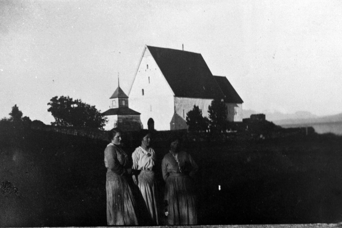 Portrett av tre kvinner stående med Trondenes kirke i bakgrunnen.
