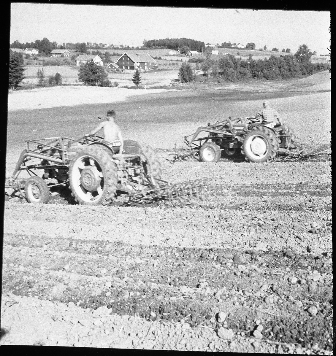 Avfotografert bilde av to traktorer som kjører våronn (harving). Stedet er ikke identifisert.