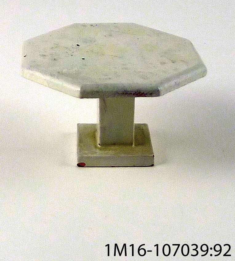 Bord till dockskåp, 8-kantigt, vitmålat, ett fyrkantigt ben i mitten på bordet samt fyrkantig benplatta.