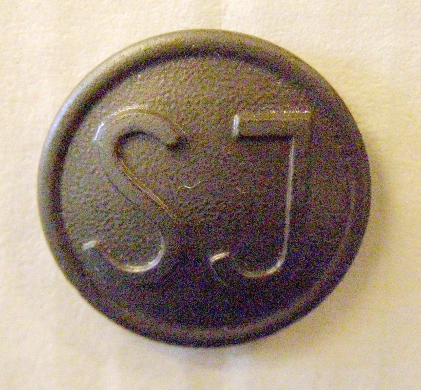 Brun västknapp med SJ:s logotyp i form av enkla initialer.