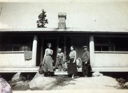 To kvinner, en mann og en gutt på trappen foran en hyttevera