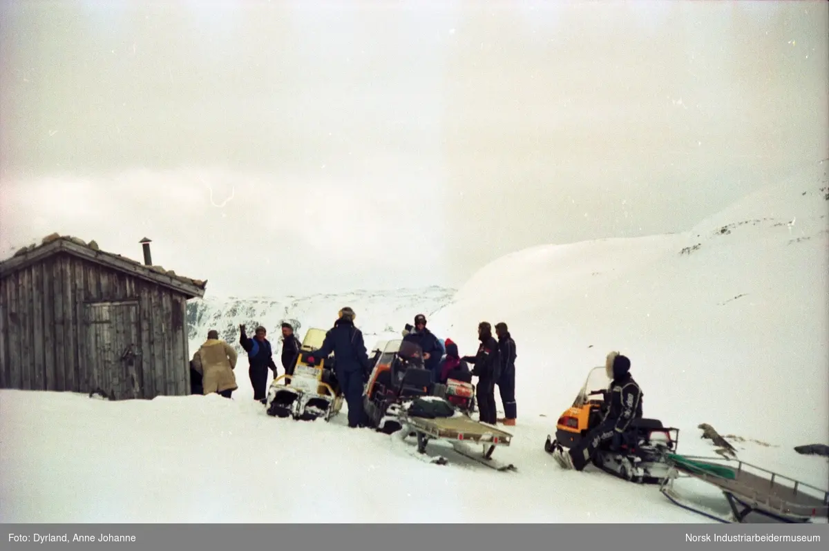 Gruppe med mennesker på fjelltur med snøskuter samlet ved hytte i fjellet