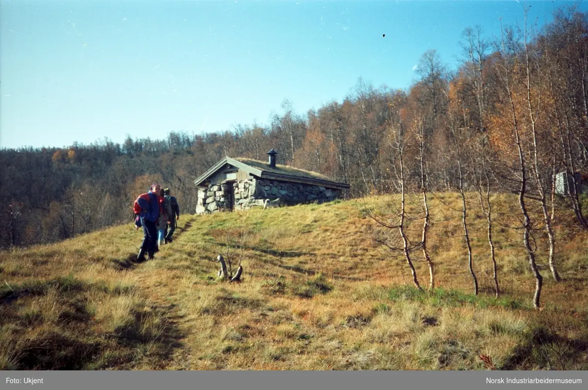Anne Dyrland med andre går på sti mot steinhytte på Haugstøl som ligger bortenfor Hovden