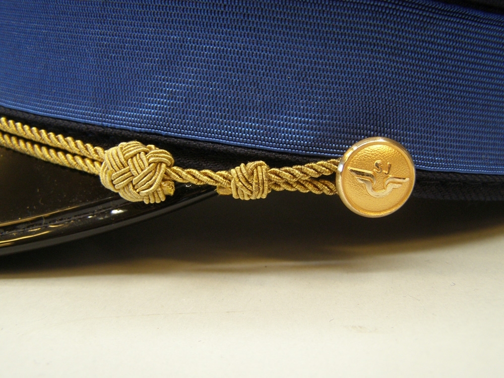 Skärmmössa med lågt kapell av vintertyg och blått mössband för tågbefälhavare.
Guldfärgad stormträns, samt guldfärgade (1991) mösstränsknappar.
Mindre guldfärgat mössmärke av 1991 års modell.