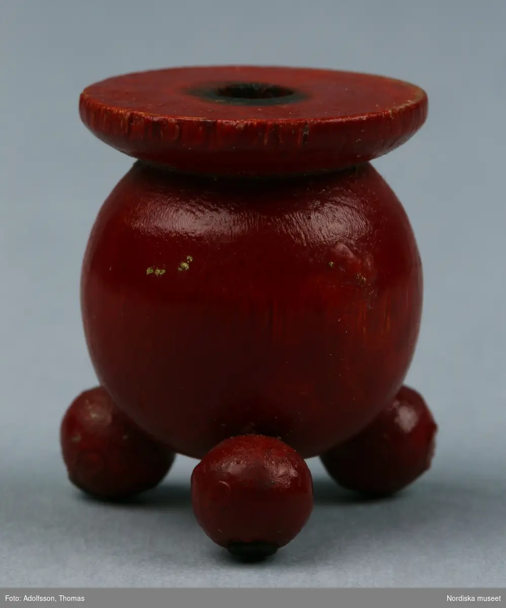 Ljusstake tillverkad av svarvade och rödmålade träkulor. Foten utgörs av tre små kulor som spikats fast vid en större kula och ovanpå denna finns en platt träskiva med ett hål (6 mm) för ett tårtljus.