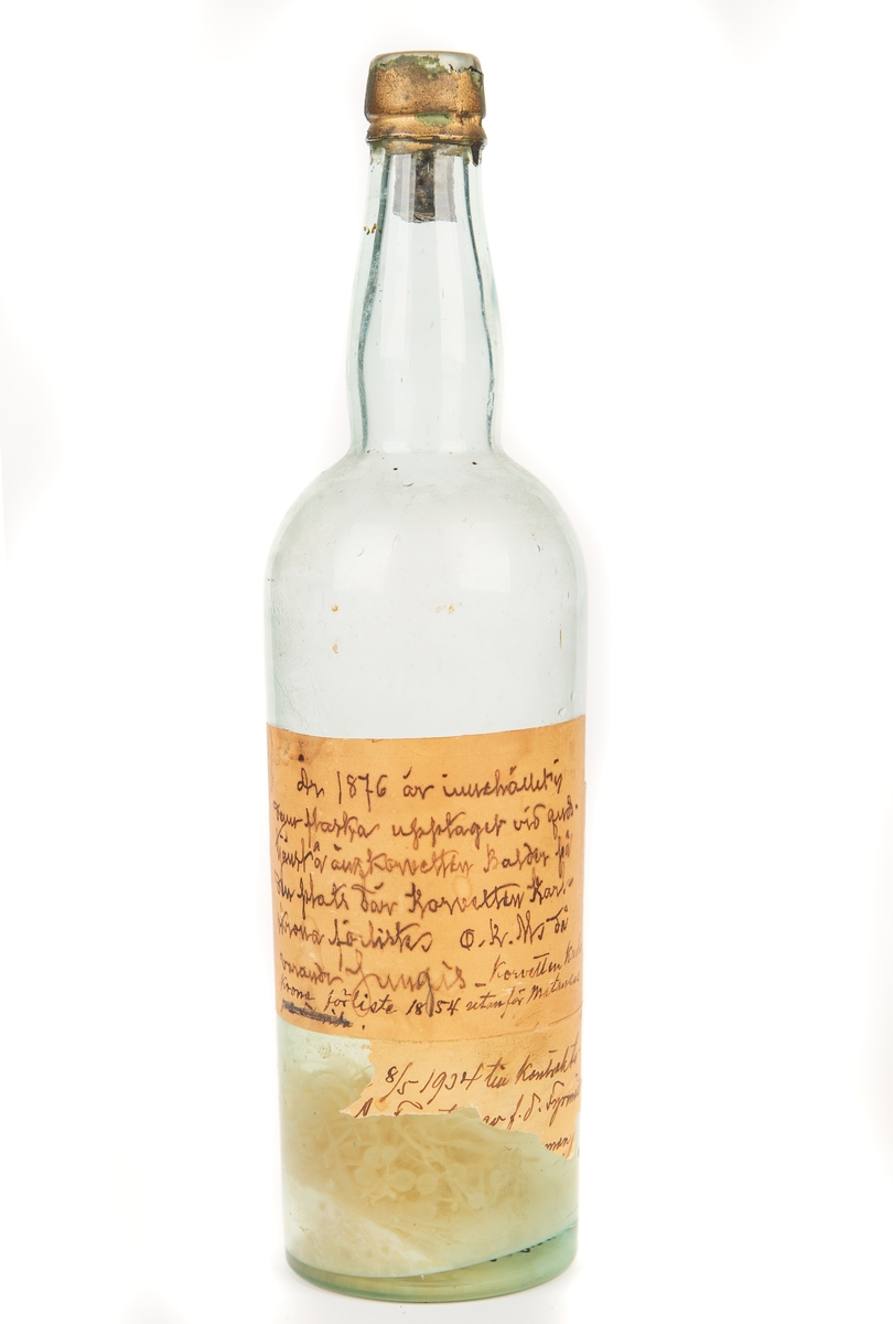 Etikett på flaskan: "År 1876 är innehållet till denna flaska upptaget vid gudstjänst å ångkorvetten BALDER från den plats där korvetten KARLSKRONA förliste. O K Ms dåvarande Jungis. Korvetten KARLSKRONA förliste 1854 utanför Maranzos 8/5 1934 till kontrakts-... av f d Fyrmäst..."
