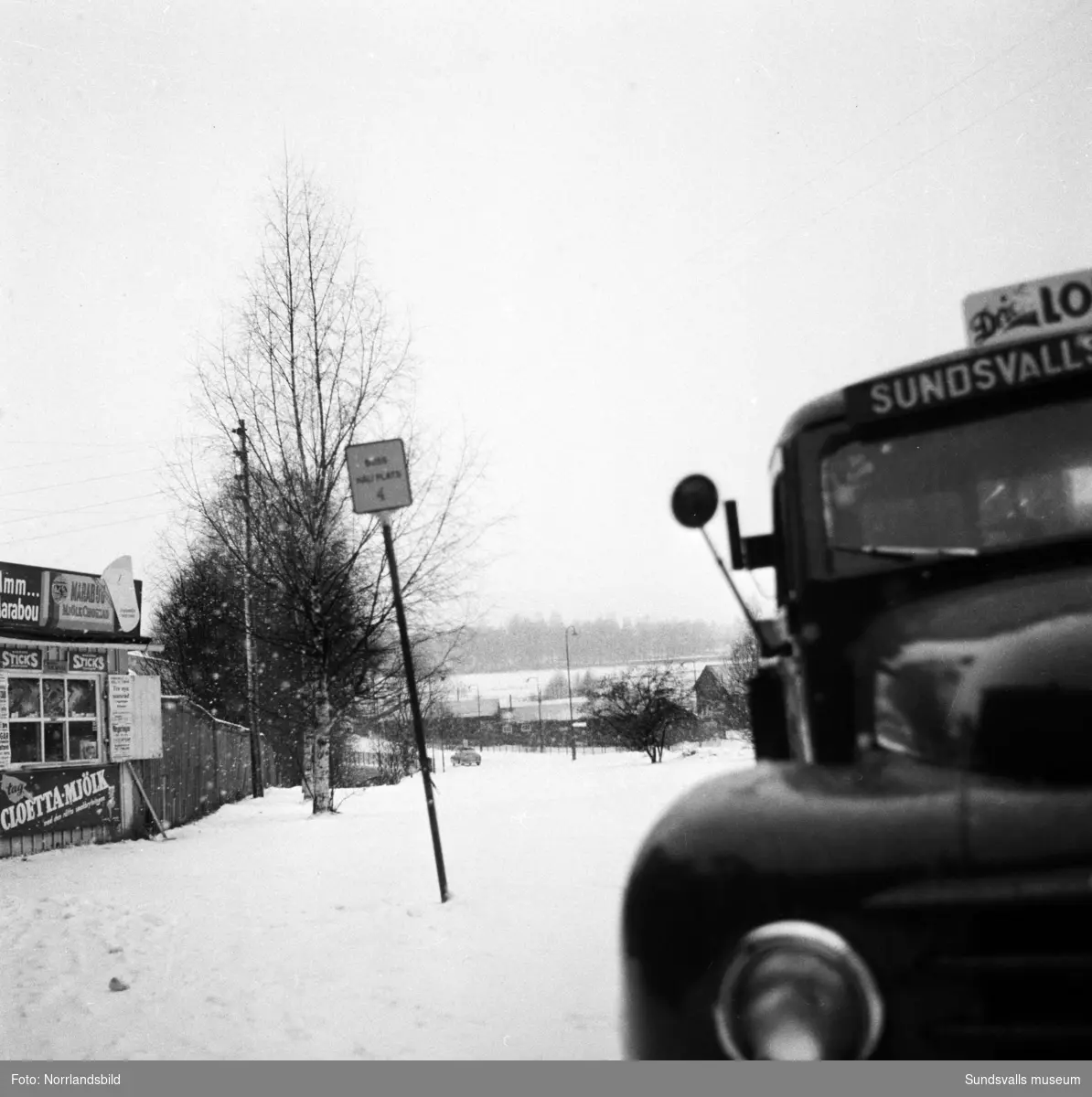 En bryggeribil i snöoväder har stannat vid en liten kiosk i korsningen av Sidsjövägen och Storgatan på Västermalm.