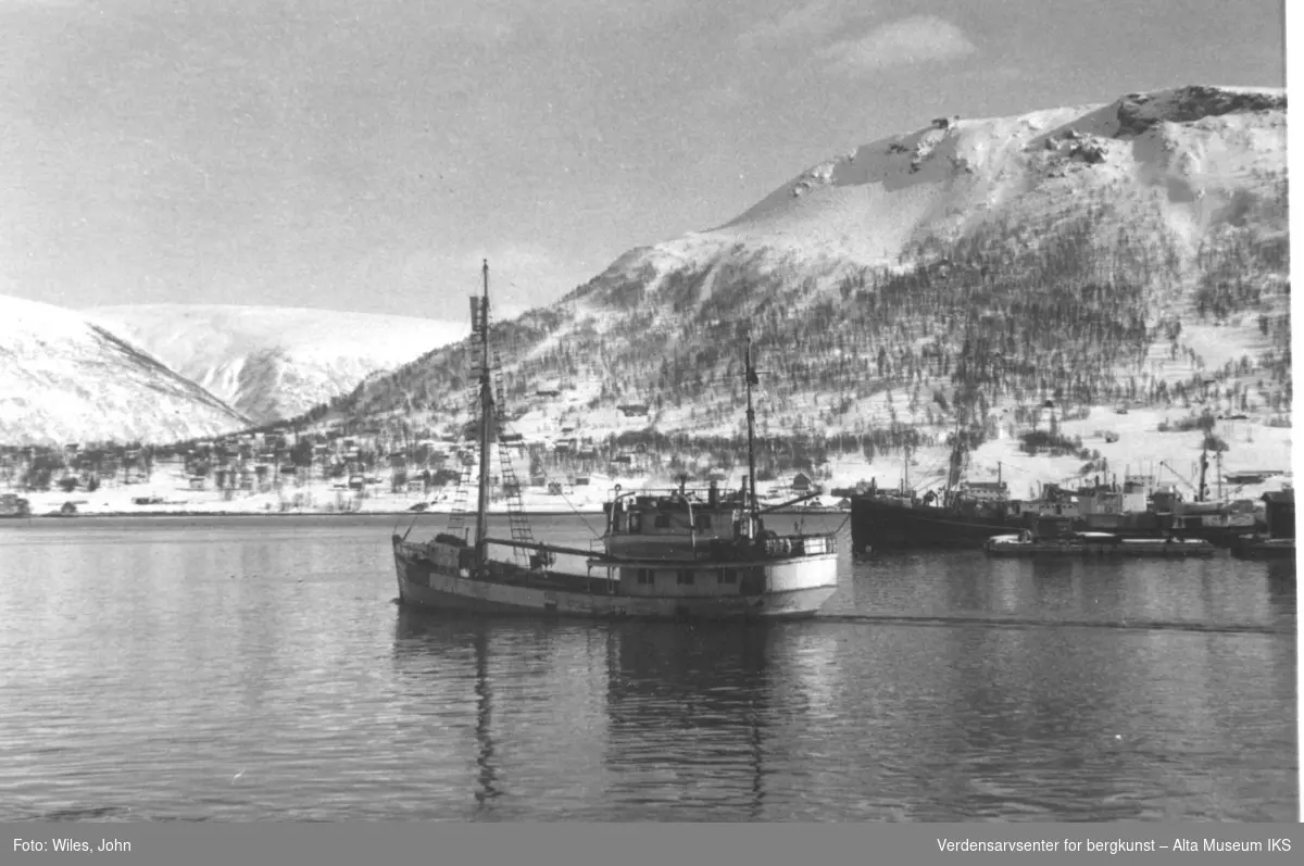 Tromsø, Ishavsskuten Polis seiler ut. Andre båter, skip og skuter ligger i bakgrunn, samt. fjell og bebyggelse.