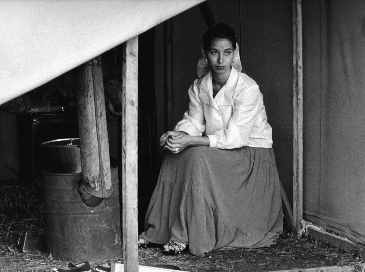 En romsk kvinna sitter i ett tält invid en hembygd kamin. Kvinnan bär dikhlo och kjol.