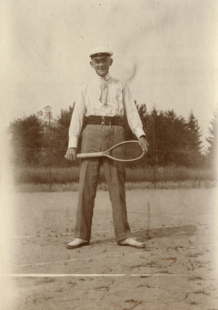 Man med studentmössa och tennisracket på tennisplan, Karlsborg sommaren 1912.