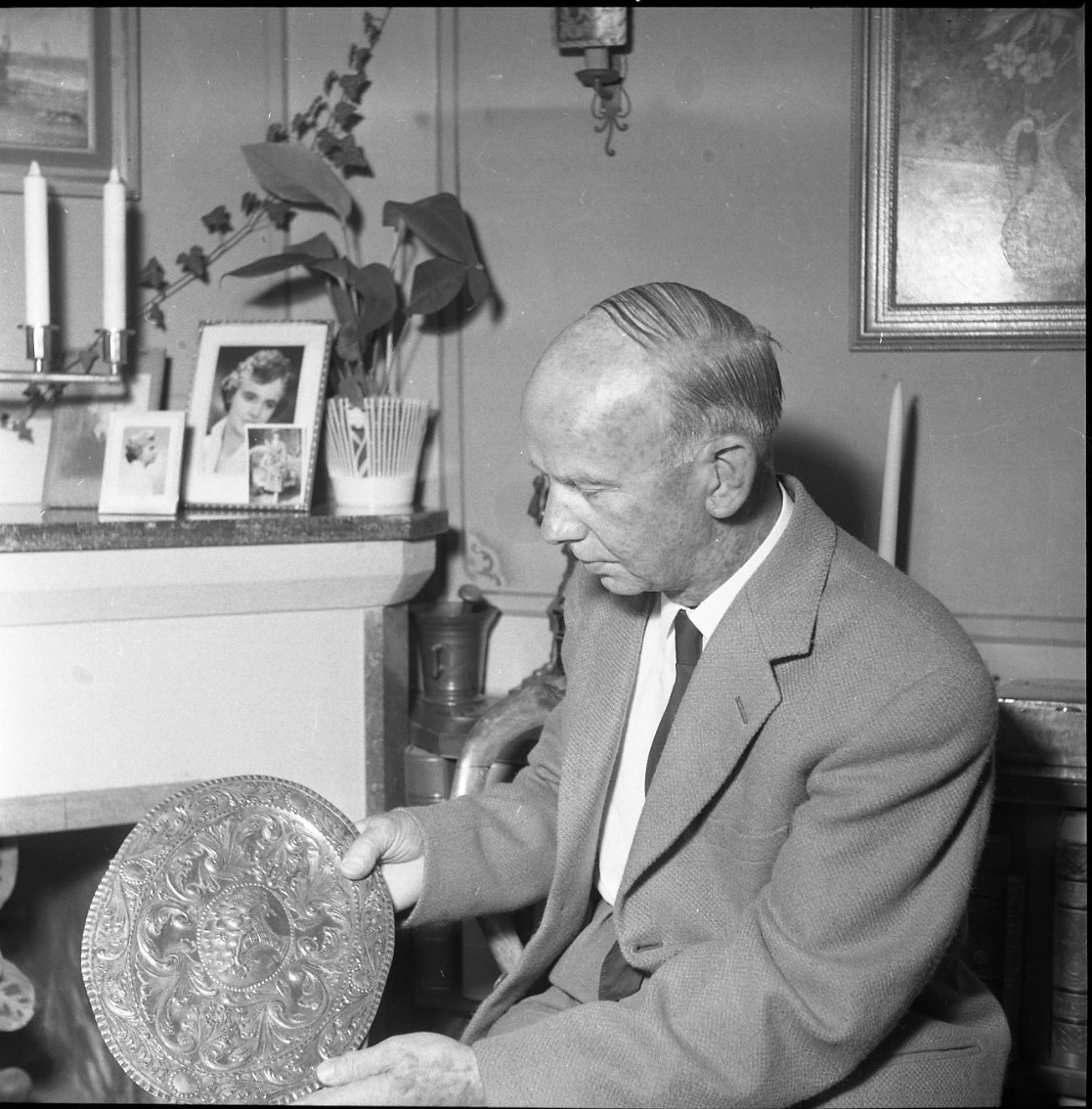 Konstsmidesmästaren Thorild Knutson sitter i sitt hem med ett ornamenterat tennfat i händerna.