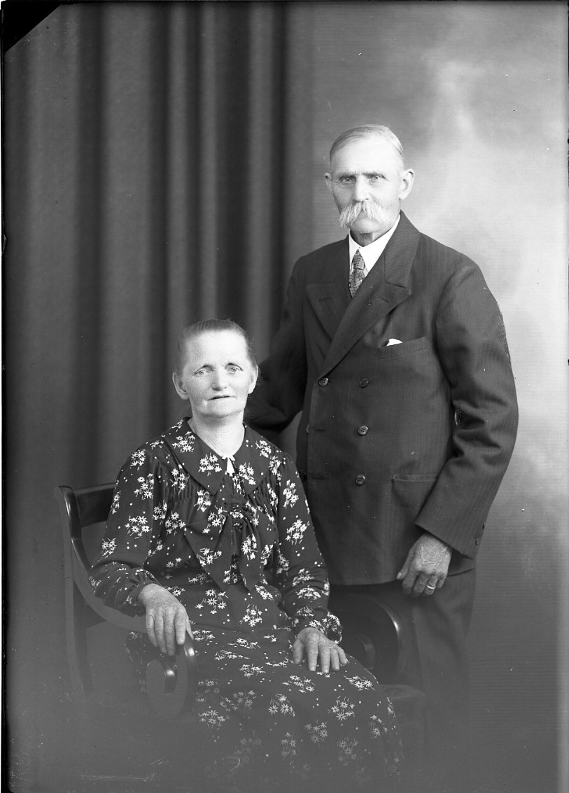 Ett äldre par vid namn Forsander. Mannen med mustasch står vid en sittande kvinnas vänstra sida. De är bägge finklädda. Hon bär en klänning med blommönster och han bär dubbelknäppt kostym med slips. Näsduk i bröstfickan.
