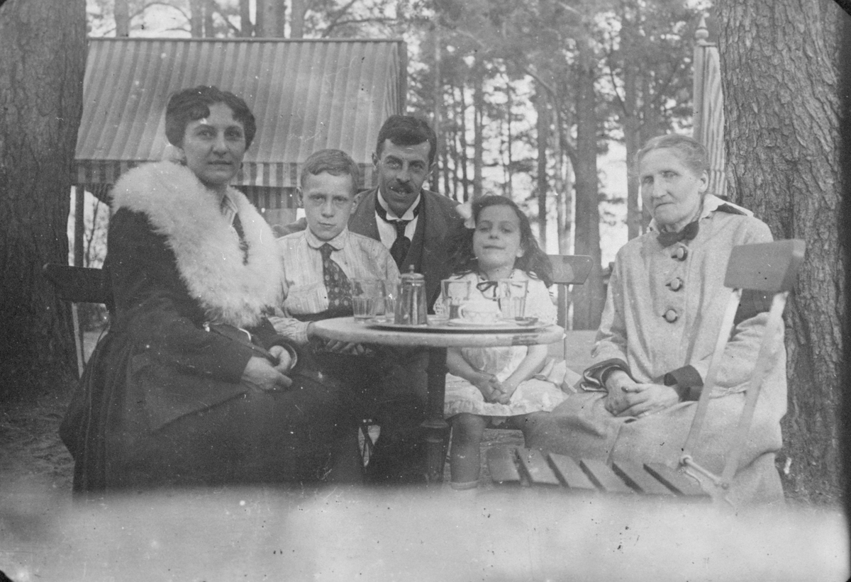 La Bella Ingeborg, Charles Bazola, dottern Hélenè och mormodern Brita Gröning runt trädgårdsbordet tillsammans med en pojke.