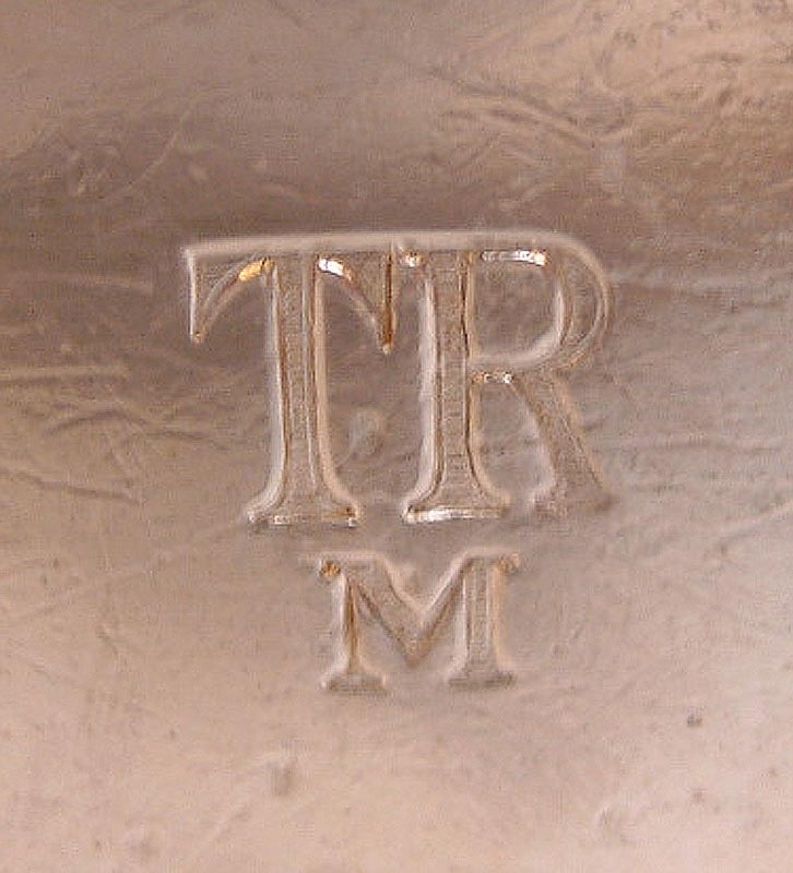 Soppskål eller terrin på fot med två öron, för 210 cl. Skålen är av nysilver med TR-logotyp med ett M under. Logotypen har ränder i bokstäverna.