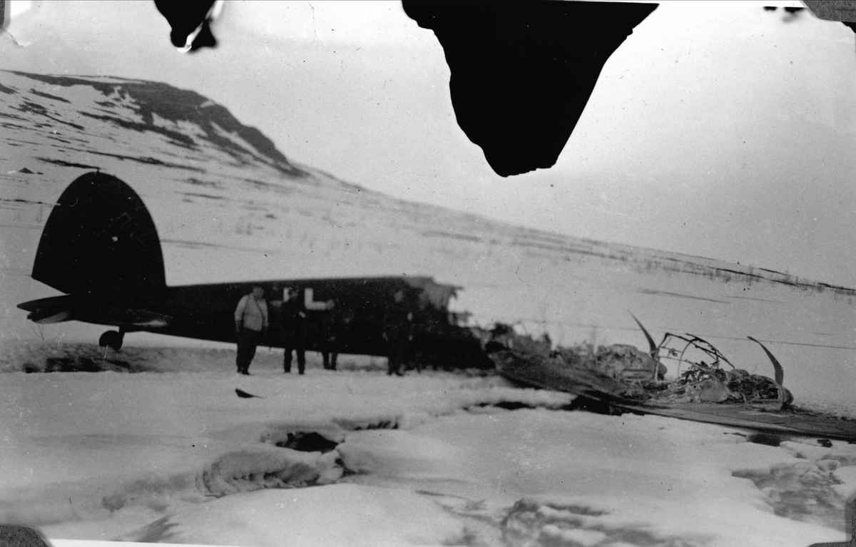 Vraket av et tysk fly i snøen oppe på et fjell. Foran flyet står det noen soldater.
