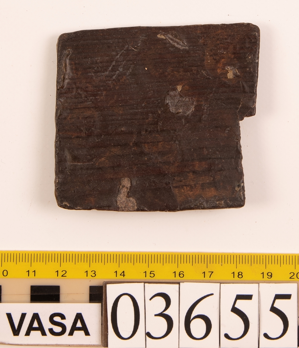 Fragment av en laggstav. Fragmentet har en avfasad flik på ena sidan. Kanten på samma sida är också avfasad.