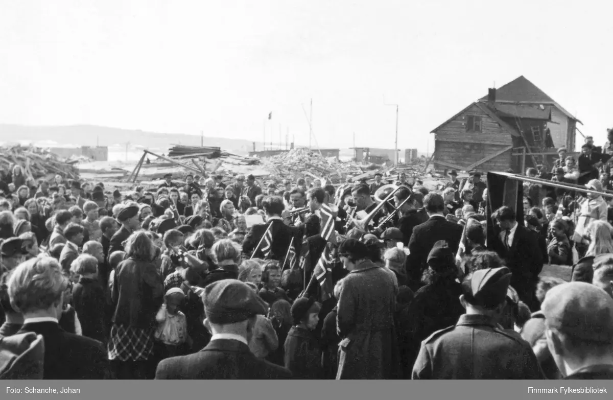 1.mai 1945 eller i 1946 i Vadsø. En folkemengde er samlet. I bakgrunnen ser vi et hus og flere ruiner etter bombinga.