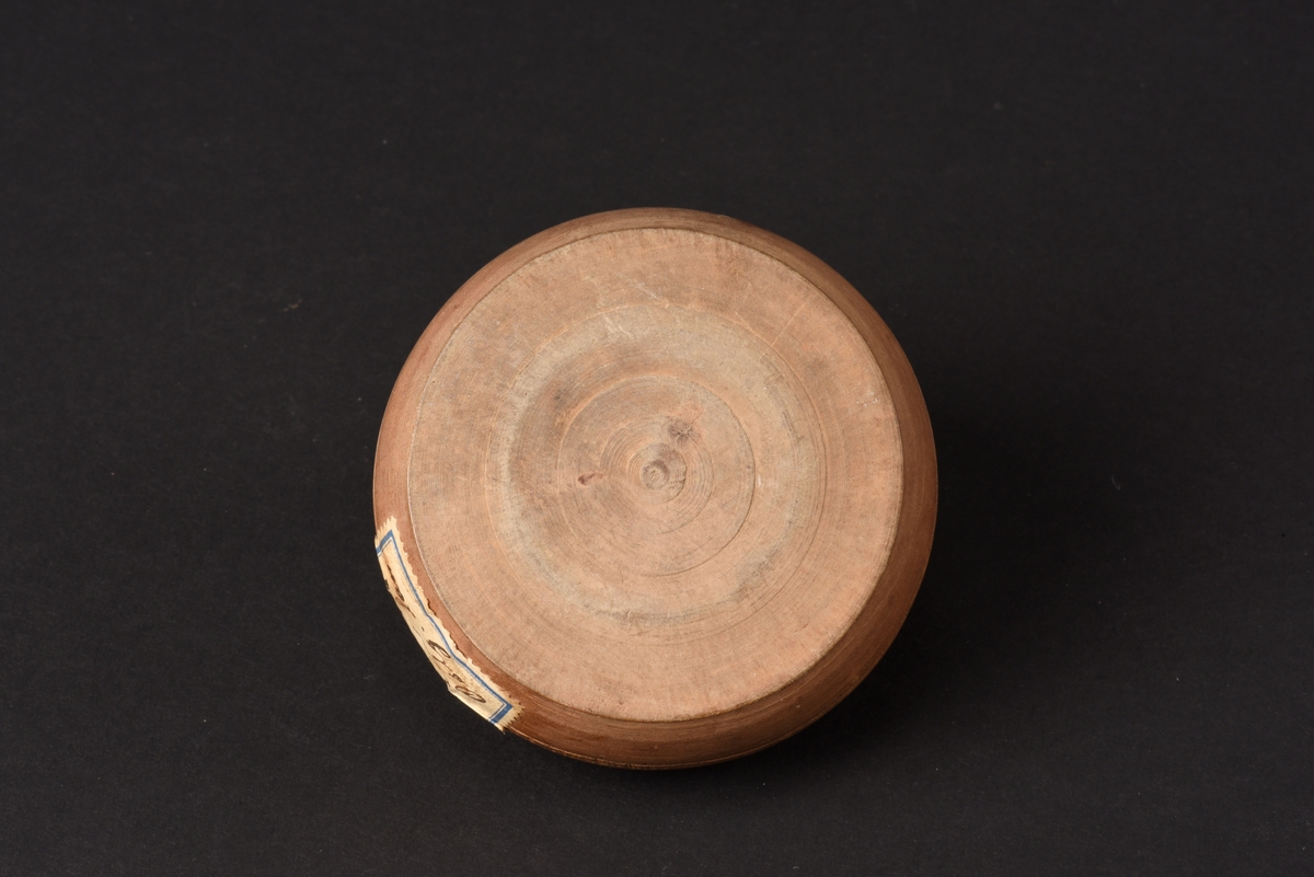 Rund svarvad smörask med lock, tillverkad av trä. Locket har ett runt svarvat knopphandtag. Det finns ett litet borrat hål på locket.