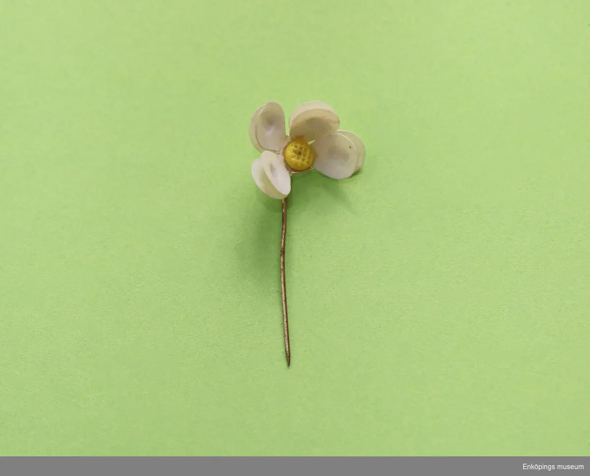 Majblomma från 1926.
Blomman är gjord av vit celluloid och har fyra blad i 2 lager, totalt 8 blad. Det tredje lagret saknas och ett blad från det översta och ett blad från det mellersta lagret har lossnat. Blomman har en gul mittknapp, även denna gjord av celluloid. Det som håller blomman samman är en nål av mässing.