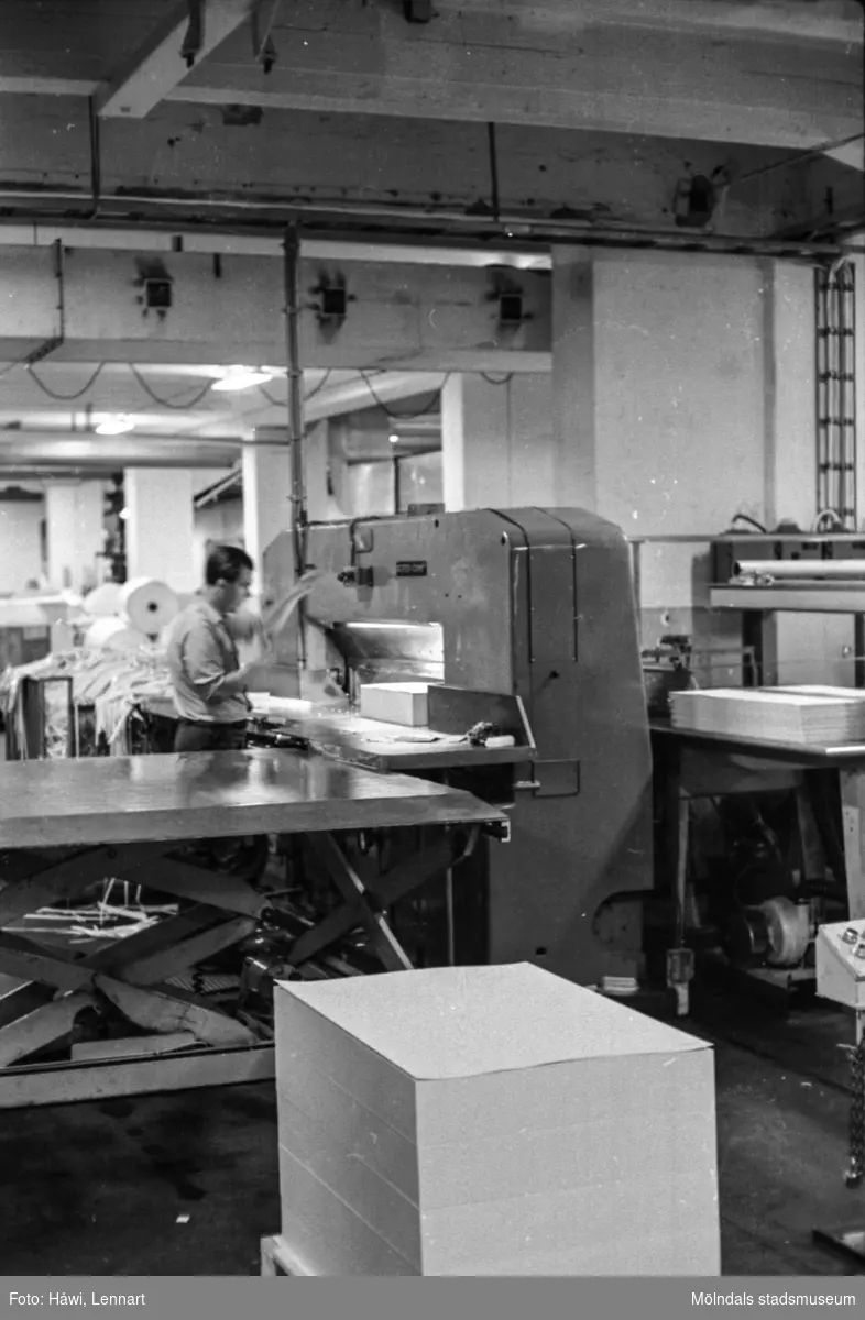 Man i arbete vid skärmaskin på pappersbruket Papyrus i Mölndal, hösten 1970. En pall med papper som kommer från klippen. Skärsalen, tredje våningen? Byggnad 18.