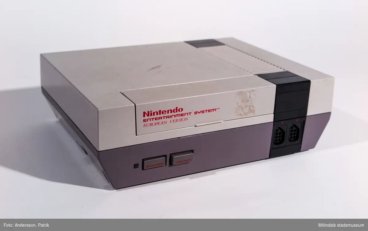 Spelkonsol för anslutning till TV-apparat. Tillverkad av vit och grå plast. Lucka i övre framkant för spelkassetter. Tryckknappar, lysdiod och anslutning av handkontroll på framsidan. 

Nätadapter NES-Pal-002 och antennomkopplare NES-003 pal.

NES, till vardags kallad Nintendo, lanserades i Japan den 15 juli 1983, i USA 1985 och i Sverige den 1 september 1986.  Konsolen baserades på kassett-teknik och 8-bitarsteknik och fick därför namnet Nintendo 8-bit.