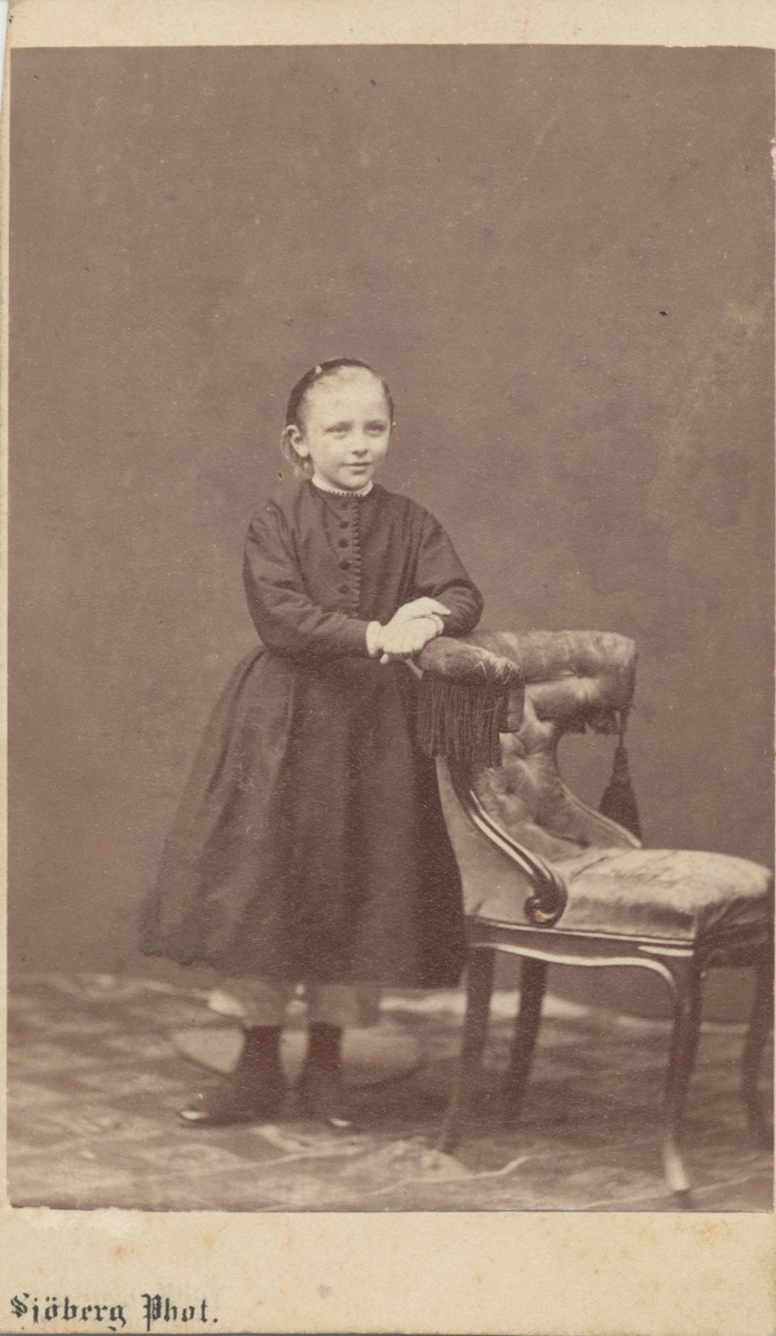 Lulli Rettig, ståendes vid en stol i studio. Robert och Adelaide Rettigs dotter.