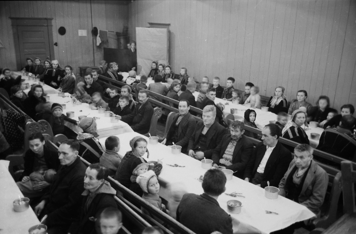 Tvangsevakuerte fra Porsanger sitter samlet til et måltid ved flere langbord og på kirkebenker i Metodistkirken i Trondheim julaften 1944. Mange av dem snur seg mot fotografen.