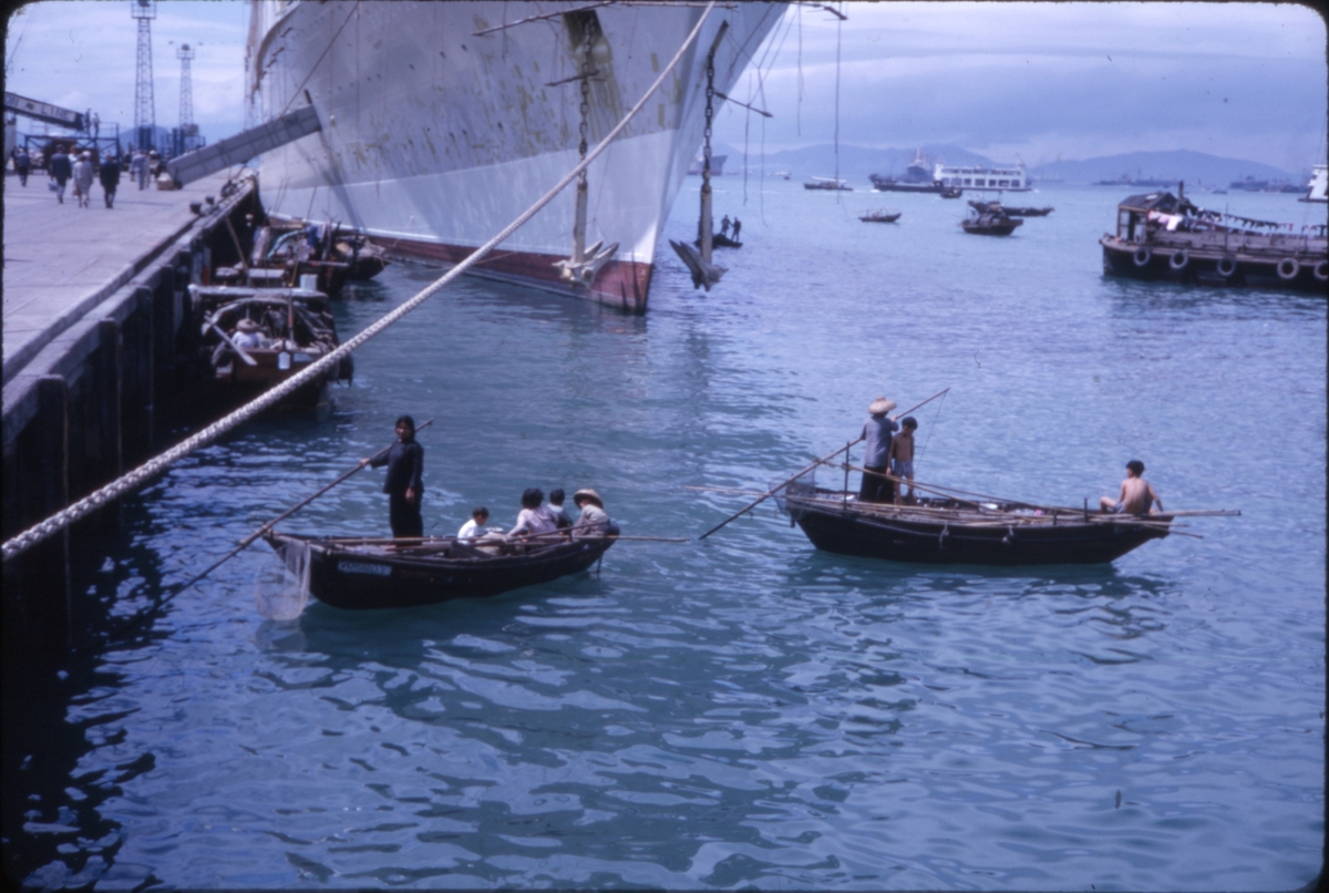 Mennesker i små fiskebåter foran større skip, trolig ved havn i Hong Kong. 'Sagafjord' Around The World via Africa Cruise 1966.