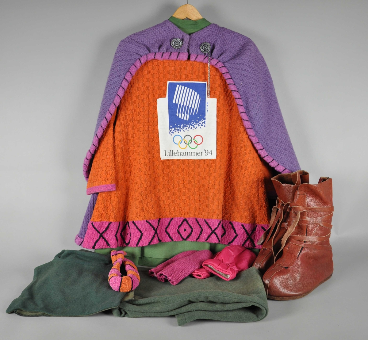 Maskotdrakt bestående av kappe, trøye med logo, kjole, bukse, hårbånd, hals (krage), votter og støvler.