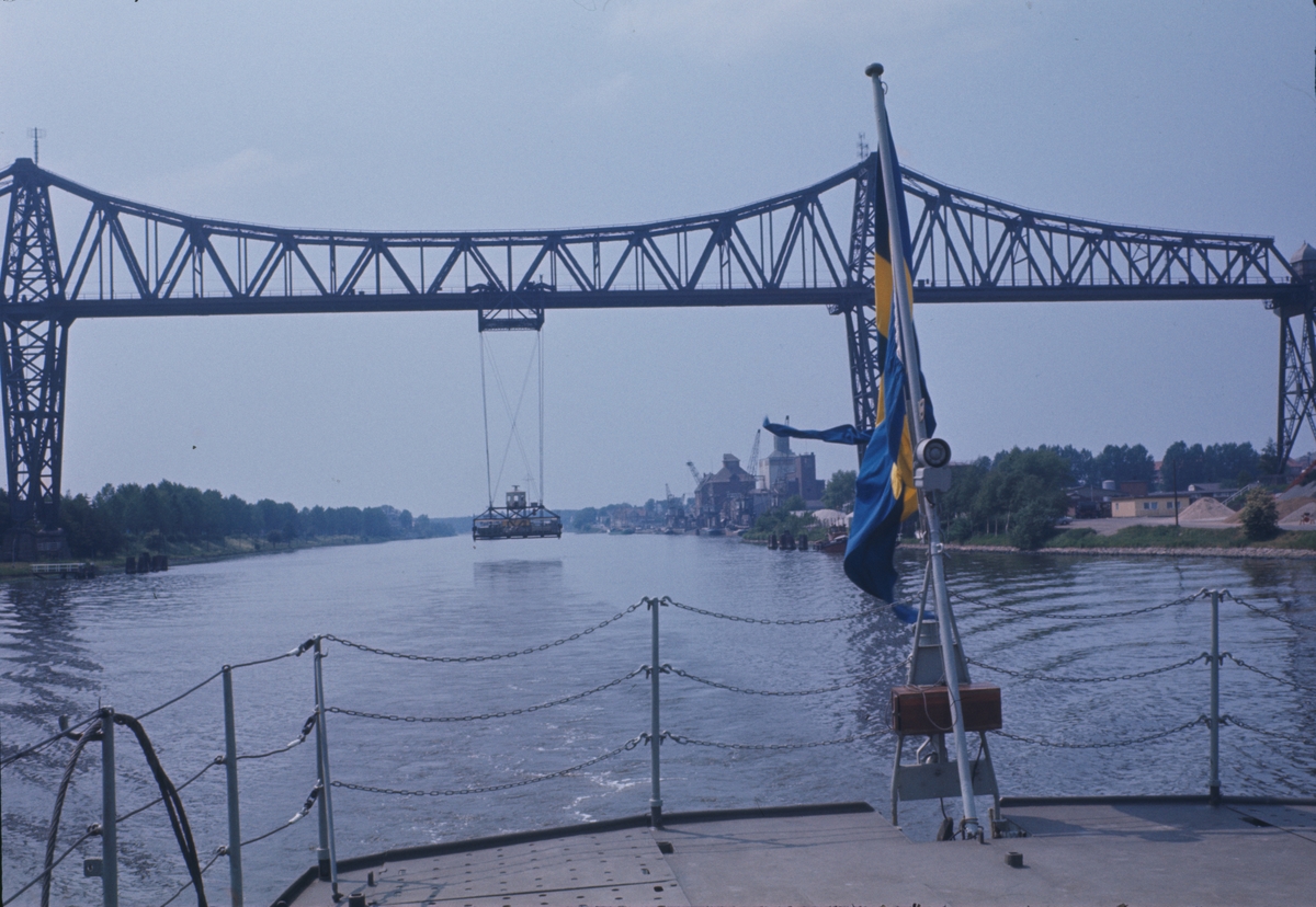 På bilden syns akterskeppet av jagaren Öland som precist har passerat järnvägsbron i Rendsburg. Under bron ser man den kända hängfärjan.